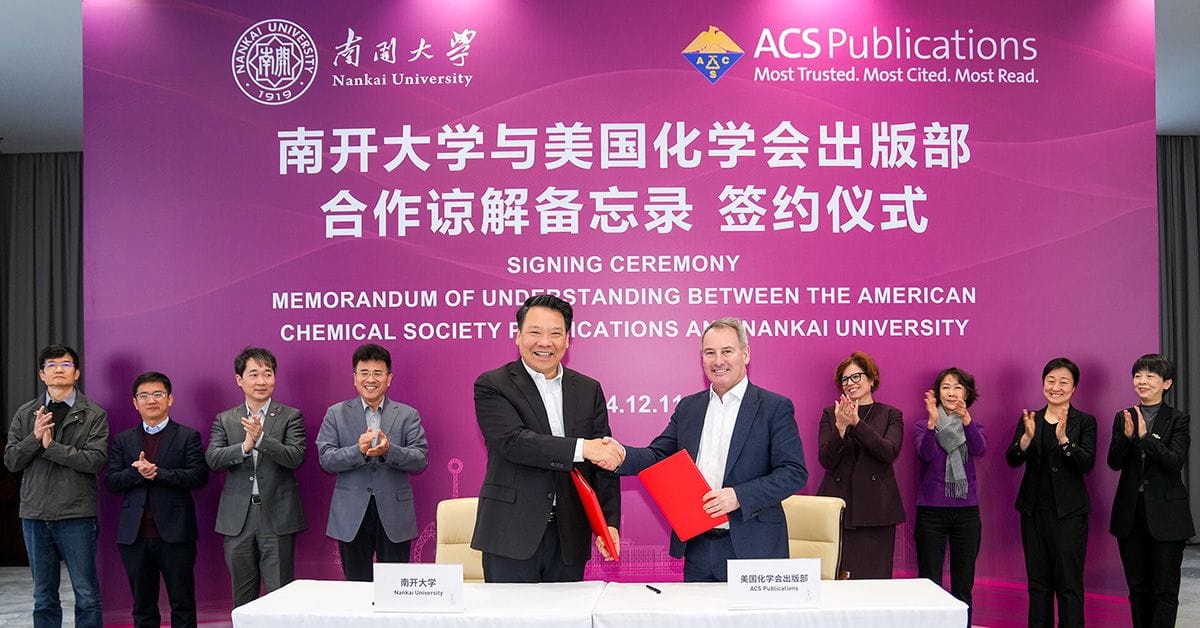 Two men shake hands at a signing ceremony for a memorandum of understanding between Nankai University and ACS Publications, with attendees clapping in the background.