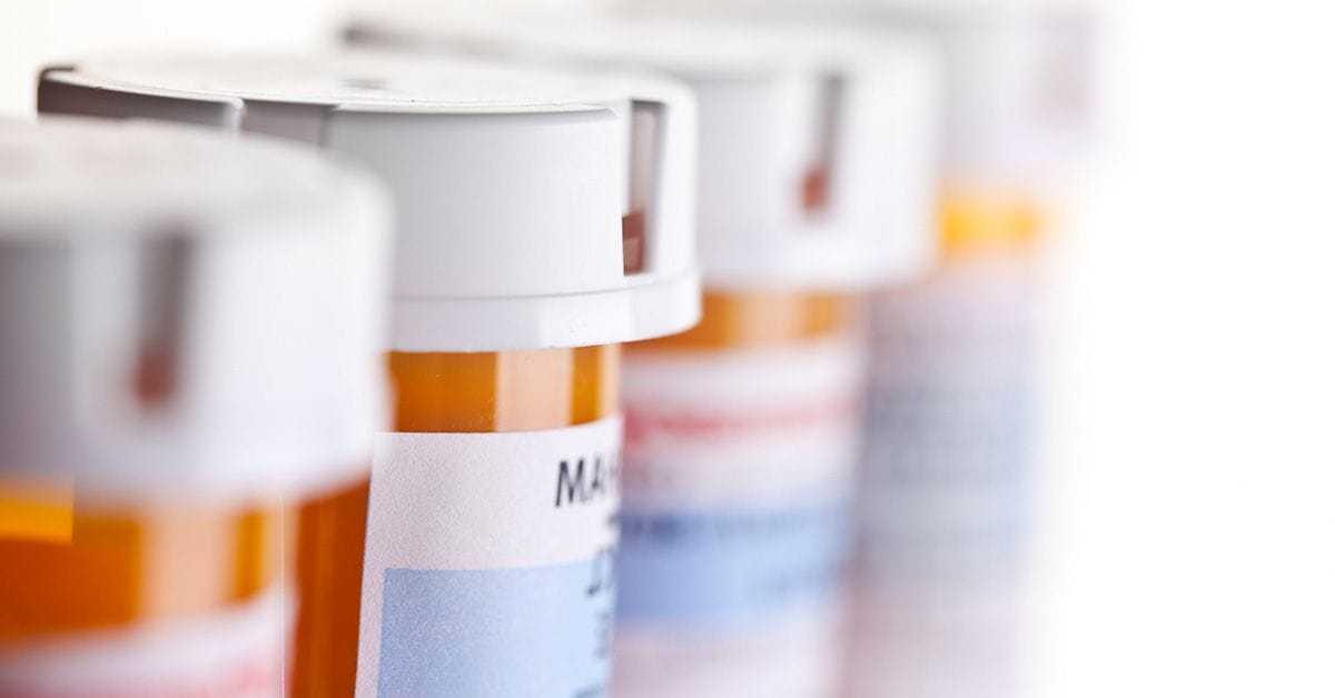 A close-up of several prescription medication bottles lined up, showcasing their white caps and colorful labels against a blurred background.