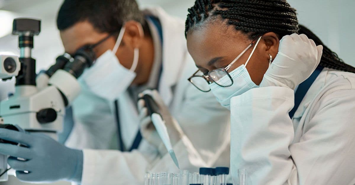 Two people in lab coats looking at microscopes.