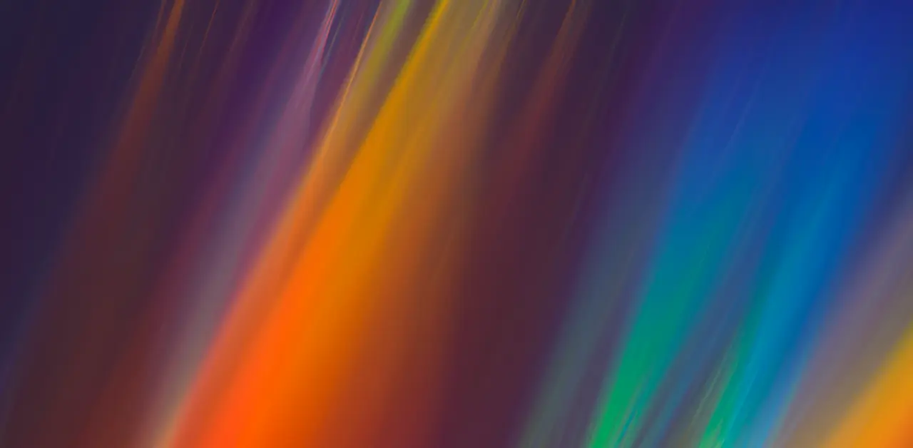 An abstract image featuring vibrant streaks of colors, including red, orange, yellow, green, and blue, on a dark background.