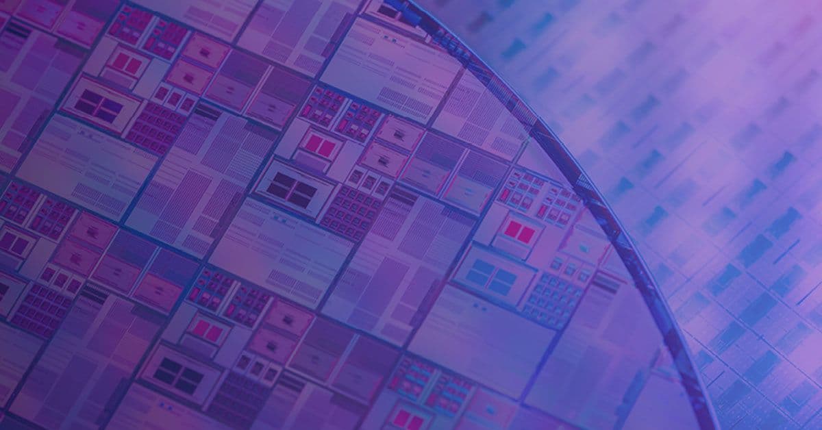 Close-up of a silicon wafer with numerous semiconductor circuits, displayed under a purple and blue light.