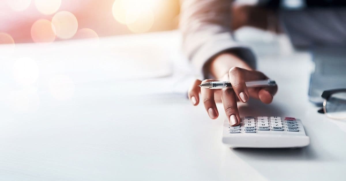 A person uses a calculator while holding a pen, with a blurred background featuring circular light flares.