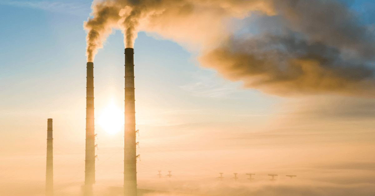 Three smokestacks from a power plant releasing pollution and smoke into the air