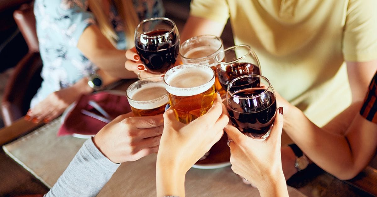 A group of friends clinking glasses of beer and wine together in celebration at a social gathering.