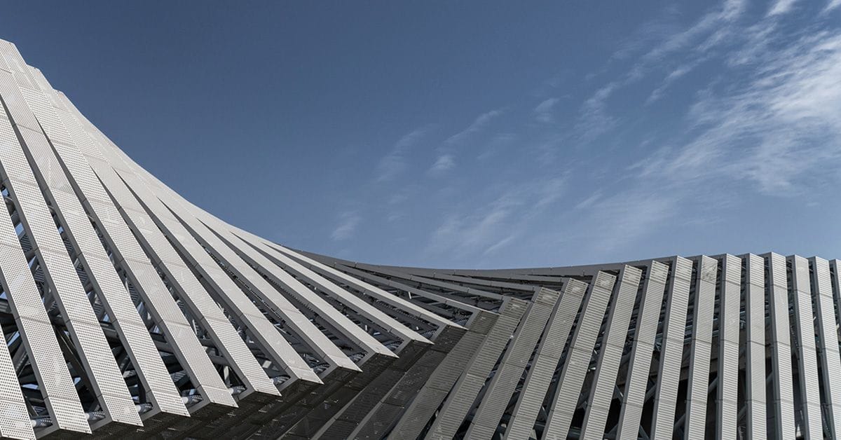 An image of a contemporary building featuring a curved design and roof, under a vibrant blue sky.