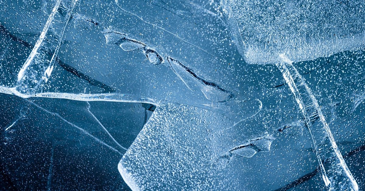 Close-up view of interconnected, translucent ice blocks with cracks and bubbles against a blue background.