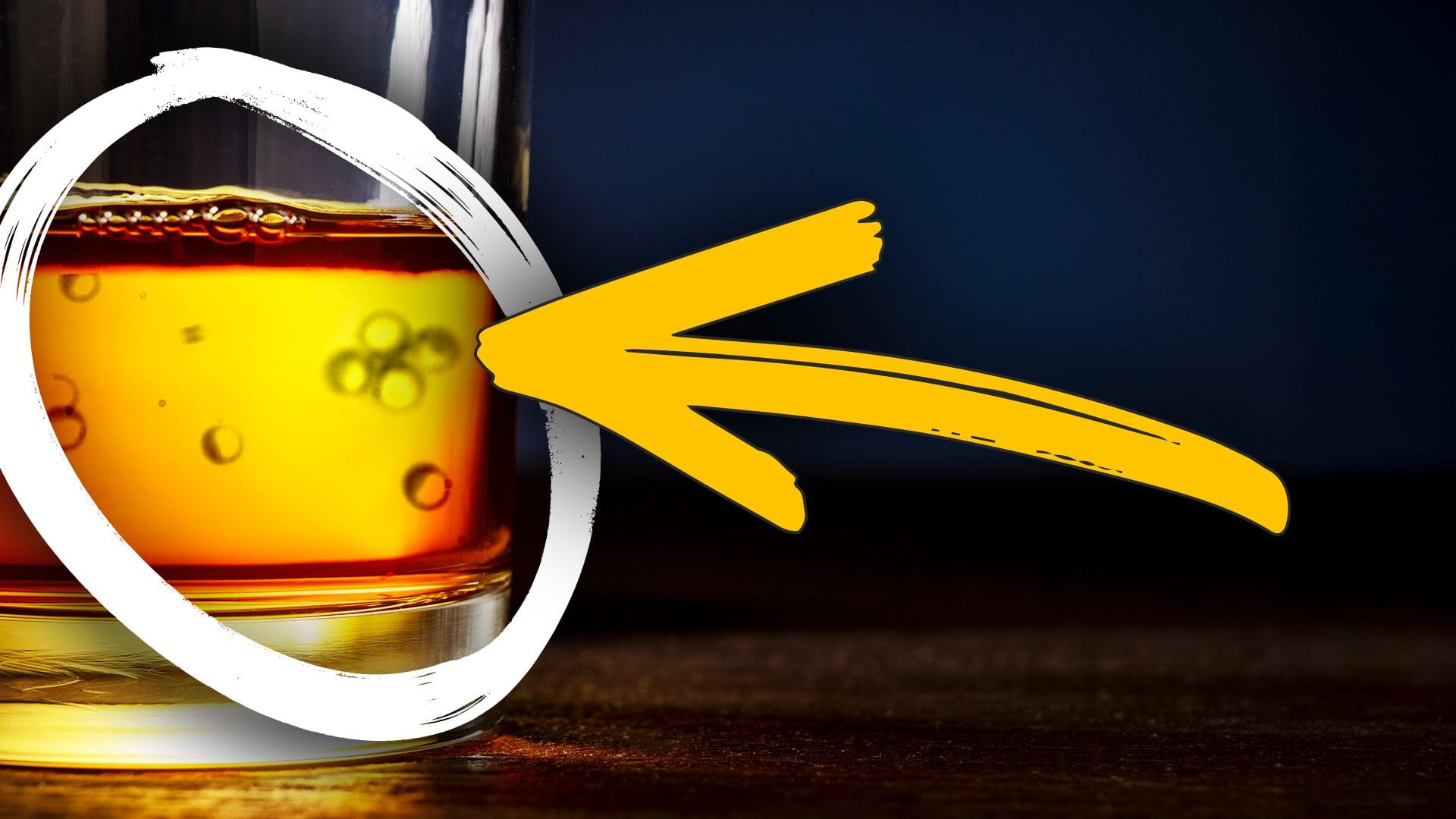 A glass of amber whisky on a wooden surface with visible bubbles or particles inside, highlighted by a white circle and a large yellow pointing arrow.