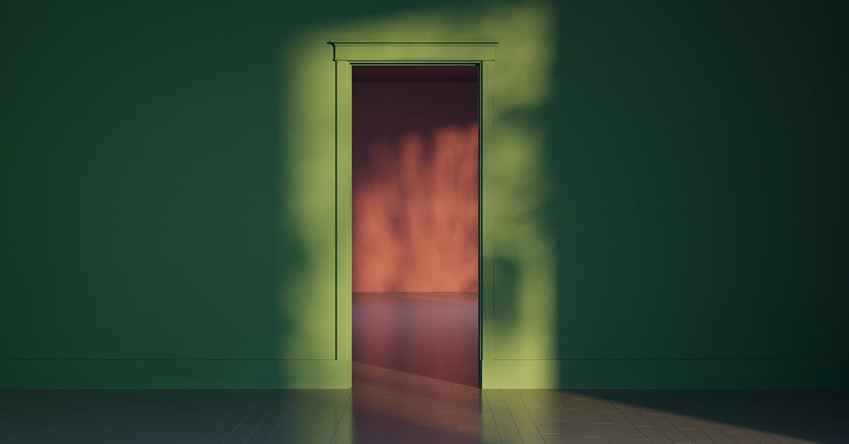 A green room with an open doorway casting warm shadows on the wall, revealing a soft orange glow from the adjacent space.