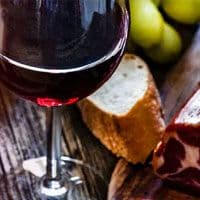 A glass of red wine and a slice of meat on a cutting board.