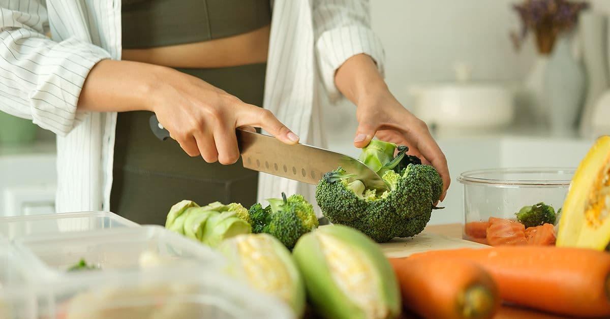 A person cutting a head of broccoli on a plastic cutting board.