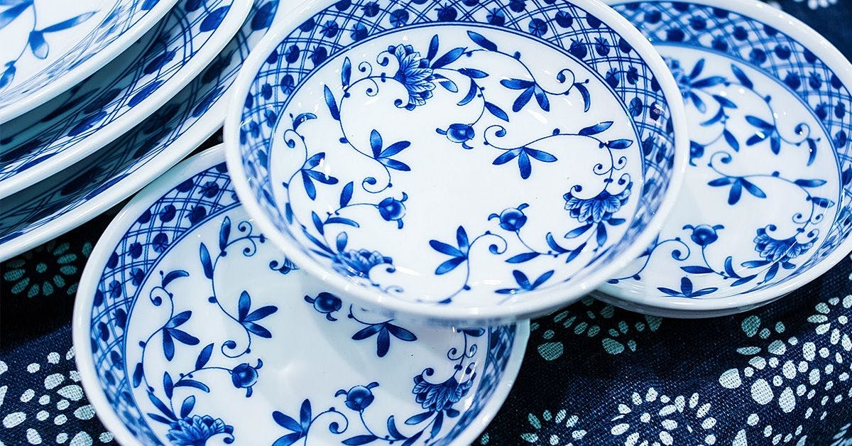 A stack of blue and white floral patterned ceramic plates and bowls on a blue textile surface.
