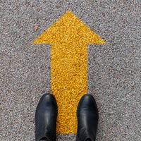 A person's feet standing next to a yellow arrow.