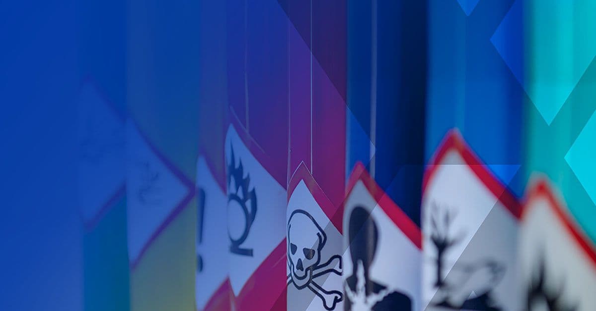 Close-up of various hazard warning signs, including symbols for flammability, toxicity, and danger, arranged in a row against a blue backdrop.