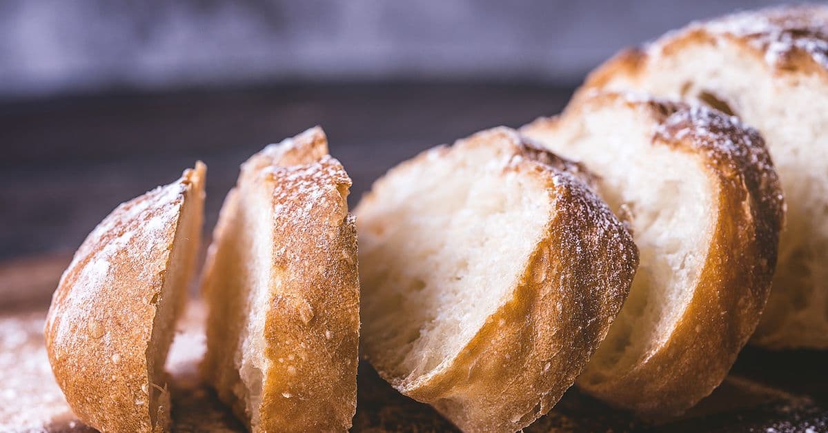 Slices of fresh sourdough bread on a floured wooden cutting board.