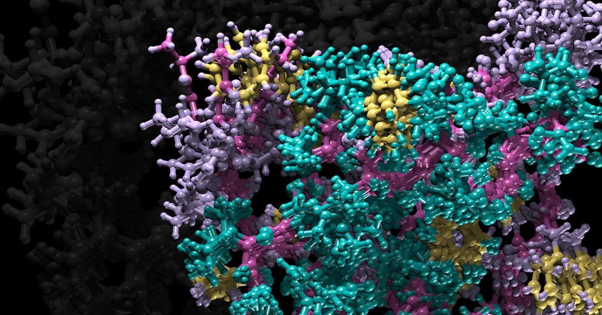 A colorful molecular structure consisting of interconnected atoms represented by pink, purple, teal, and yellow spheres against a dark background.