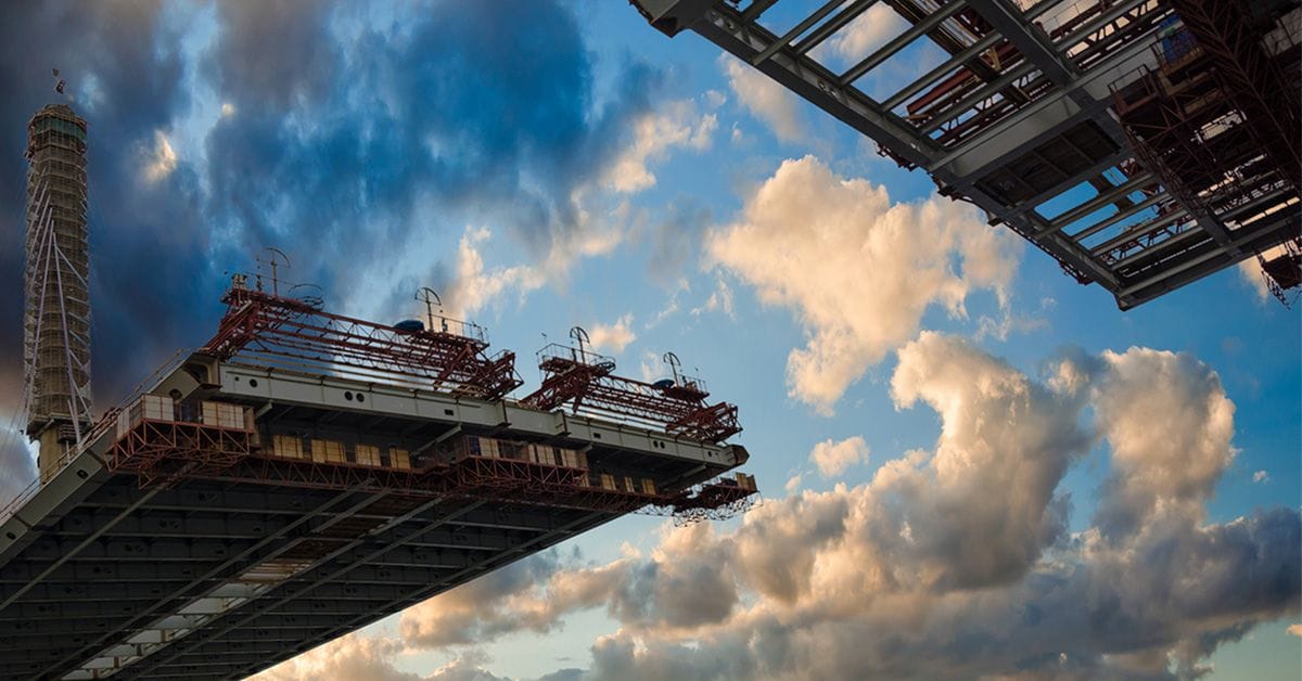 Two large structural beams extend from a construction site, framed against a backdrop of dramatic clouds and blue sky.