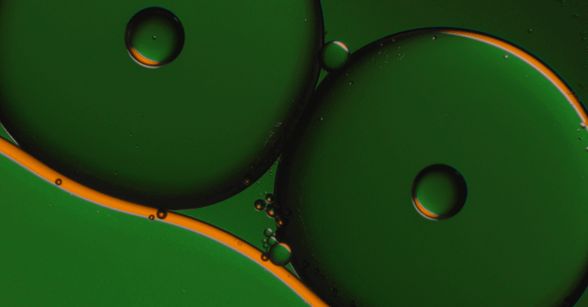 Macro photograph of overlapping circular oil bubbles in deep green, rimmed and connected by bright orange-gold light, with tiny clustered droplets in the center.