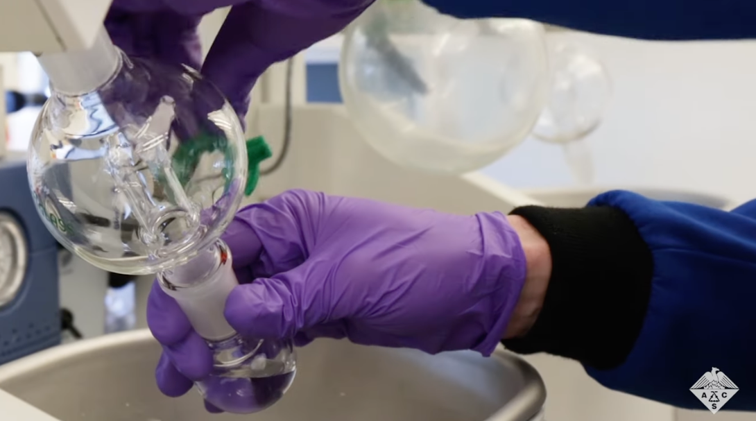 A person wearing purple gloves handling laboratory glassware.