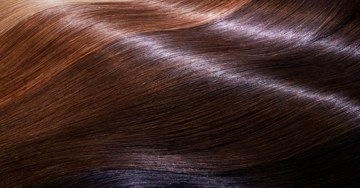 Magnified view of healthy hair fibers in various shades of brown, with smooth texture and reflective sheen, illustrating hair structure or surface properties.