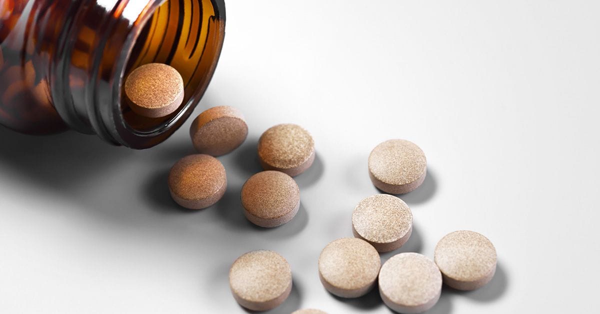A brown glass pill bottle tipped over with several round beige tablets scattered on a white surface