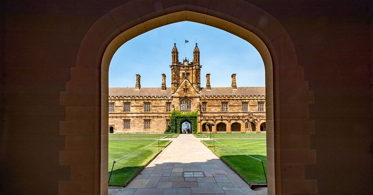 An image of a stately campus building and grounds, visible and framed through the opening of a corridor archway