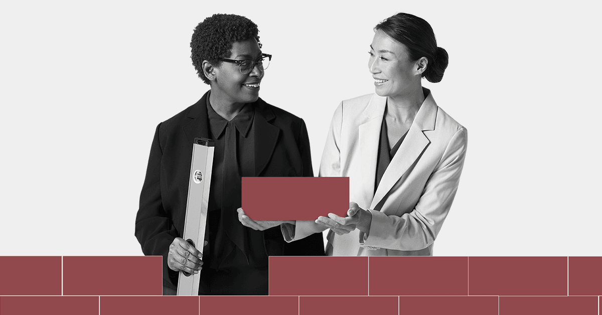 Two women standing next to a brick wall holding a piece of paper.