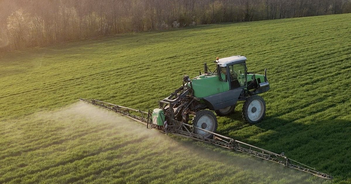 A green tractor sprays chemicals across a lush green field under a warm, glowing sunlight, enhancing agricultural productivity.