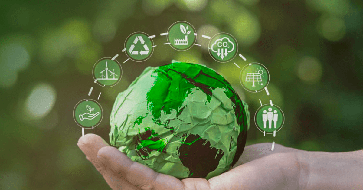 A hand holds a green paper globe surrounded by eco-friendly icons.