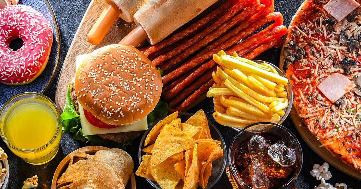 A spread of junk food, including donuts, pizza, chips, fries, burgers, and soda