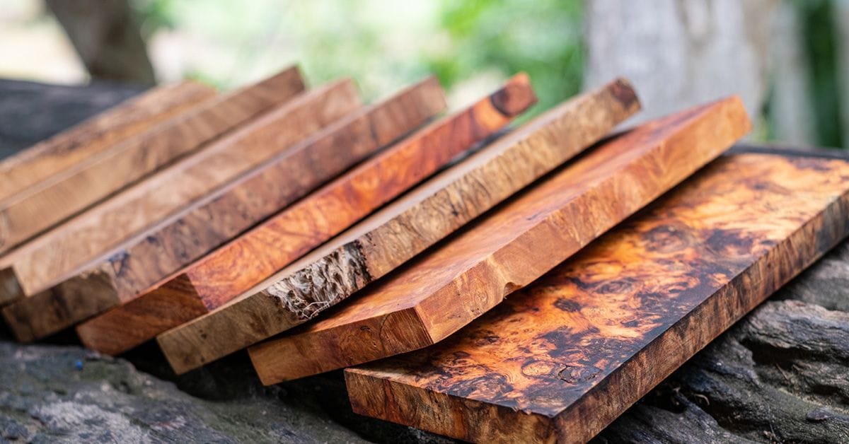 Several pieces of polished wooden boards with distinct grain patterns are arranged on a dark outdoor surface.