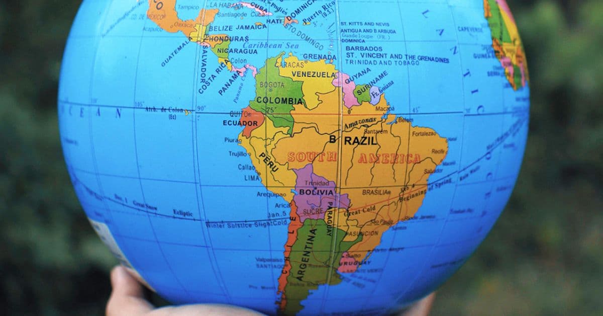 A person holds a globe showing Latin American countries, featuring countries like Brazil, Colombia, and Argentina in vibrant colors.